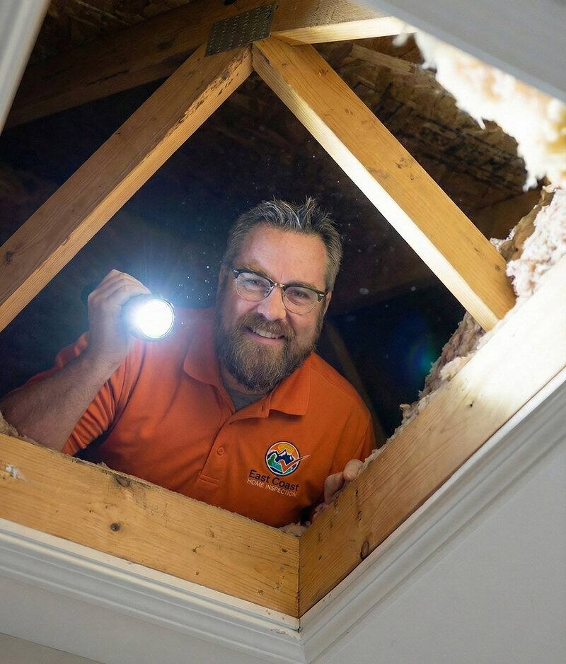 Home inspector in an attic with a flashlight, checking for moisture