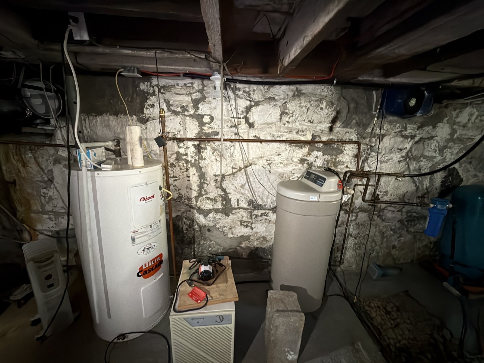 A water heater, water softener, and dehumidifier running against a stone foundation wall in an older Southern New Brunswick basement