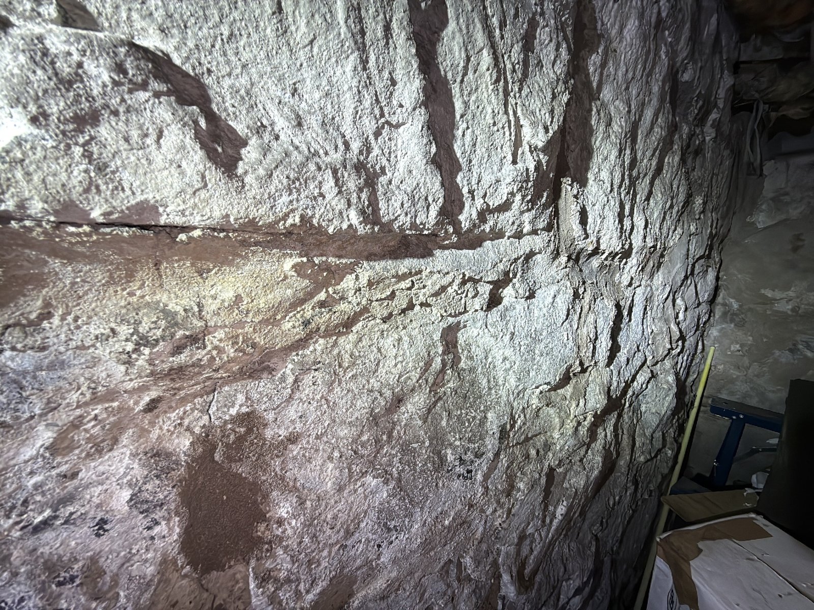 A flashlight held against a stone foundation wall to check the condition of the mortar joints up close during an inspection