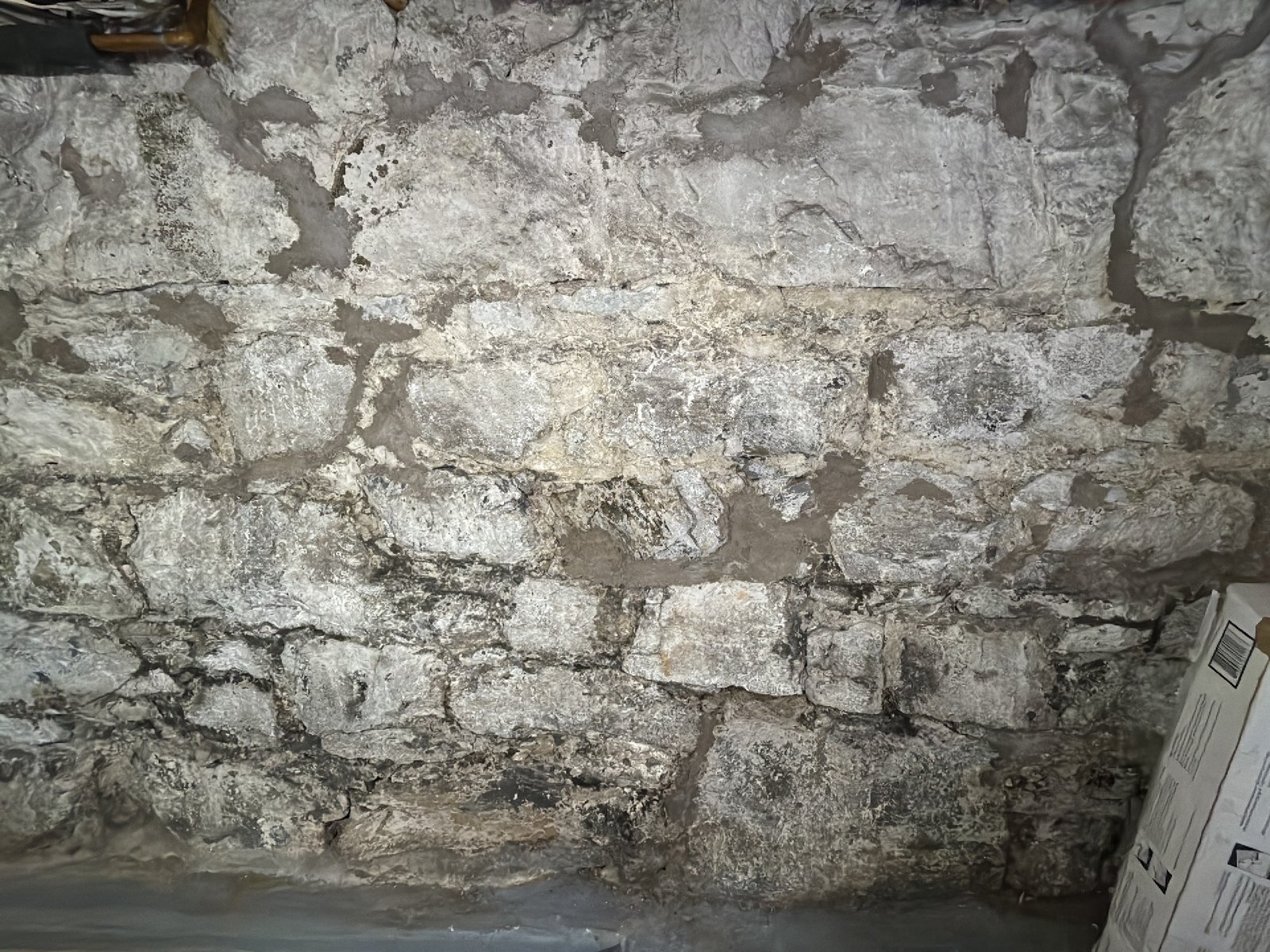A whitewashed rubble stone foundation wall with older cement patches over the original lime mortar joints, seen during a Southern New Brunswick home inspection
