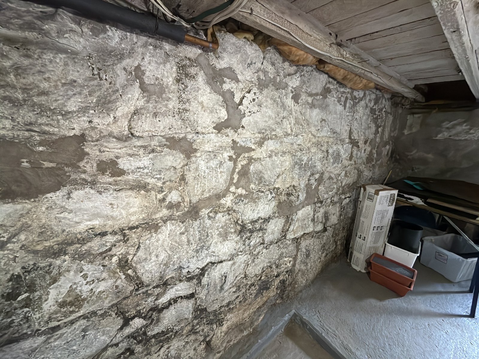 A rubble stone foundation wall meeting the original hand hewn floor joists in an older Southern New Brunswick basement, photographed during a home inspection