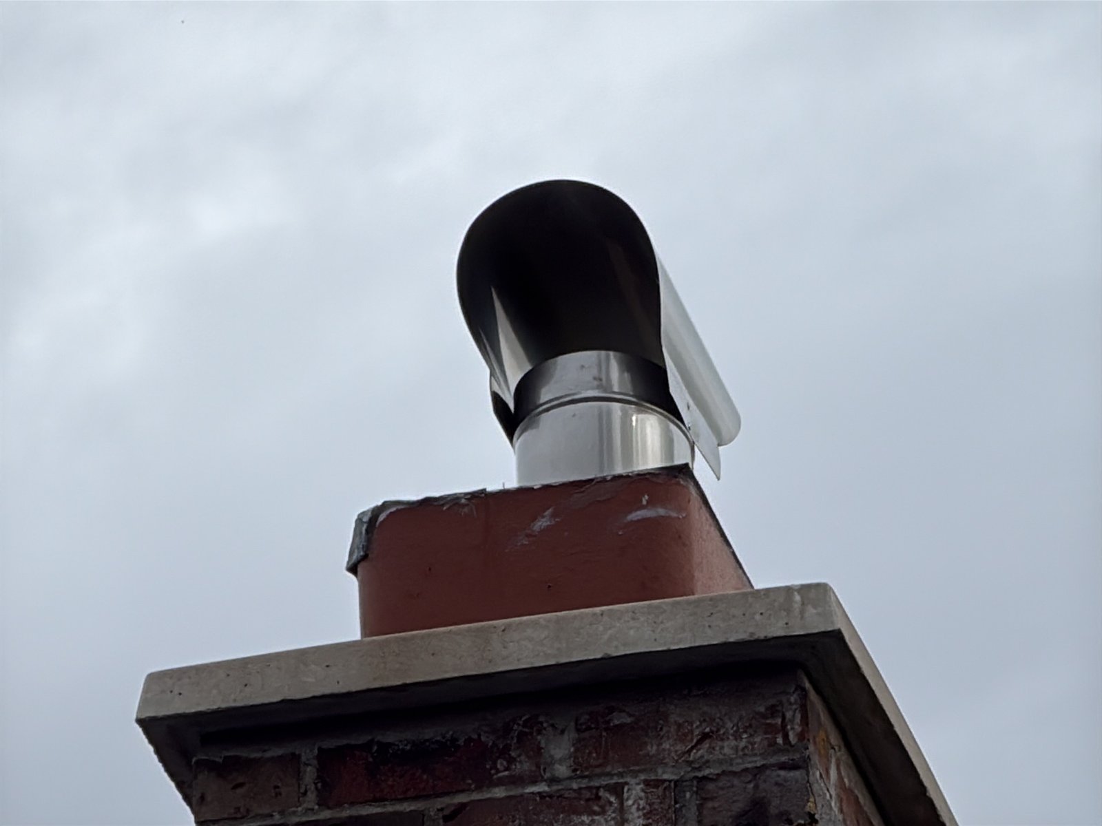 A stainless steel liner rising out of the clay flue tile of a brick chimney, finished with a hooded rain cap
